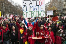 A demonstrator holds a poster that reads 'State of Climate Emergency' behind Indigenous people during a protest in Paris, France, on December 12, 2015 [Etienne Laurent/EPA]